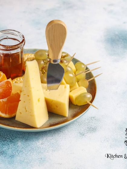 A simple yet elegant cheese plate featuring wedges of hard cheese, fresh grapes, and orange slices, served with a small jar of honey. This highlights the classic and timeless pairing of cheese and fruit.
