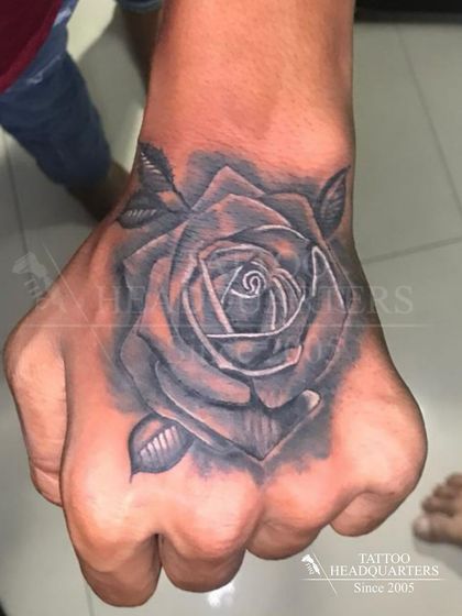 A realistic black and grey rose tattoo on the hand, with deep shading that makes the flower pop.