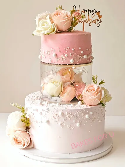 Celebrating 30 years of love with this stunning Pearl Anniversary cake. This three-tier design features a clear separator filled with fresh flowers and lights, surrounded by delicate pearl details.