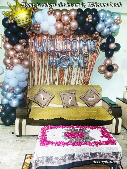 Nothing says "we missed you" like a beautiful welcome home surprise. This setup features a stylish balloon arch in rose gold, black, and silver, complete with a crown foil balloon and a table centerpiece of fresh rose petals.