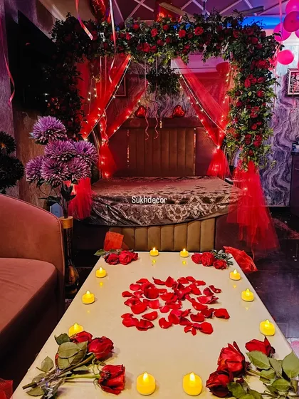 This image focuses on the small details that make the setup special. A table is decorated with scattered red rose petals and surrounded by warm, flickering battery-operated candles for a safe and romantic ambiance.