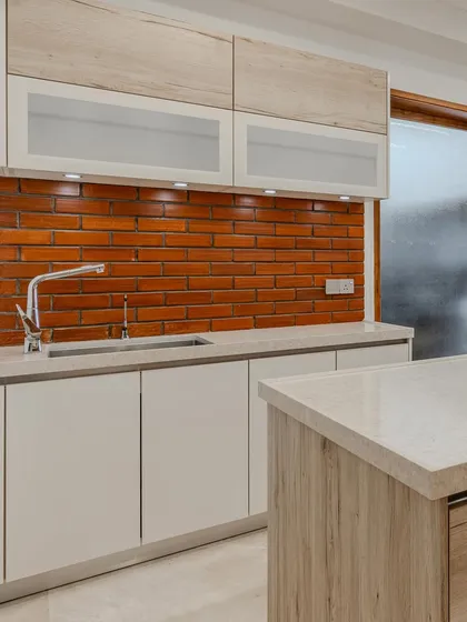 A detailed shot of the sink area, where the earthy brick backsplash meets the clean lines of the Kalingastone countertop and handleless cabinets, showcasing a beautiful contrast of textures.