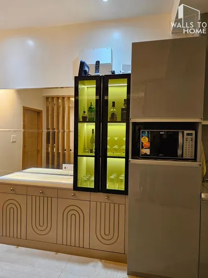 A minimalist crockery and bar unit integrated with the kitchen. The design features a lit glass cabinet for display, a built-in microwave, and handleless base cabinets with a routed arch pattern.
