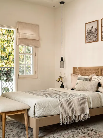 This guest bedroom highlights the timeless appeal of cane furniture and a light, airy color scheme. The window opens to the lush greenery outside, and the design is kept simple to create a peaceful and welcoming space for visitors.