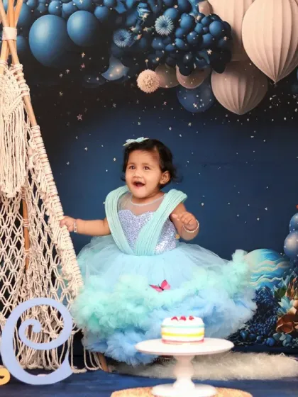 A princess celebrates her first birthday, twirling in a beautiful gown against a magical night-sky backdrop with balloons and a teepee.