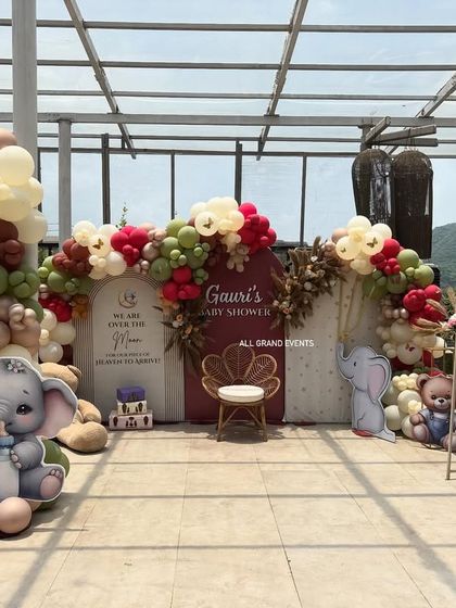 A wide shot of the entire baby shower setup on a rooftop, showing the main backdrop flanked by balloon columns and large elephant cutouts.