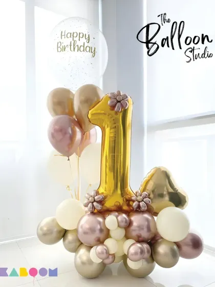 An elegant and stylish balloon bouquet for a first birthday, featuring a gold number one with rose-gold and cream-colored balloons for a chic celebration.