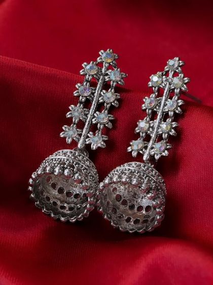 A pair of silver jhumka earrings on a rich red silk cloth. The contrast between the silver and red creates a bold and dramatic look.