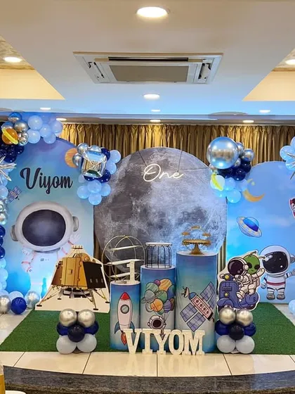 An out-of-this-world space theme for a first birthday party. This full setup includes a custom moon and planet backdrop, astronaut and rocket ship props, and a galaxy-inspired balloon arrangement to create an unforgettable adventure.