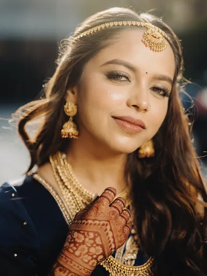 A beautiful close-up of this bride's glowing skin and traditional gold jewelry. The makeup is kept warm and neutral to complement the rich blue of her saree and the intricate henna design.