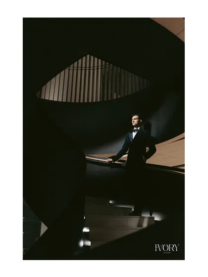A portrait of the groom, exuding confidence and style. The play of light and shadow on the spiral staircase creates a moody, cinematic, and powerful image.