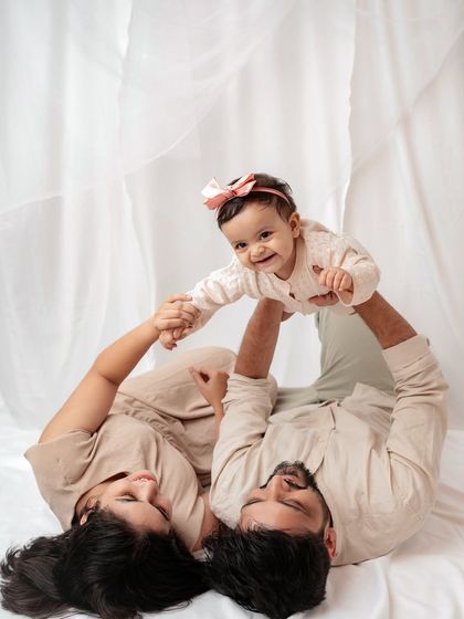 A playful family moment, with the parents lifting their baby in the air.