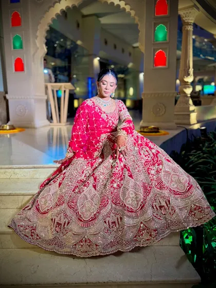 A full-length shot of a bride in her magnificent red lehenga, her hair styled in a secure floral bun. This showcases how a classic updo complements a grand bridal outfit perfectly.