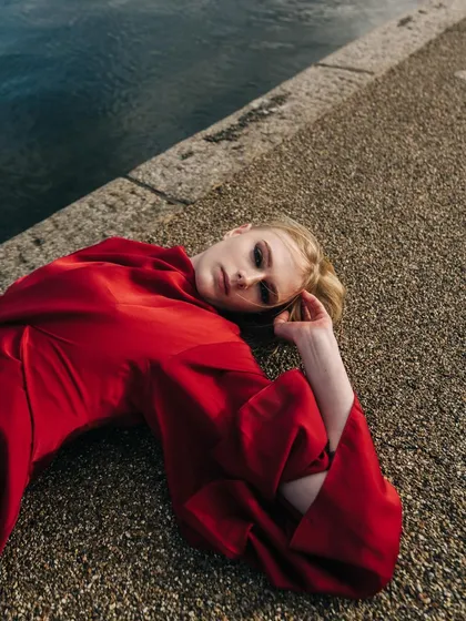 An overhead shot of a model in a red dress lying on the concrete edge of a lake, creating a strong contrast of color and texture.