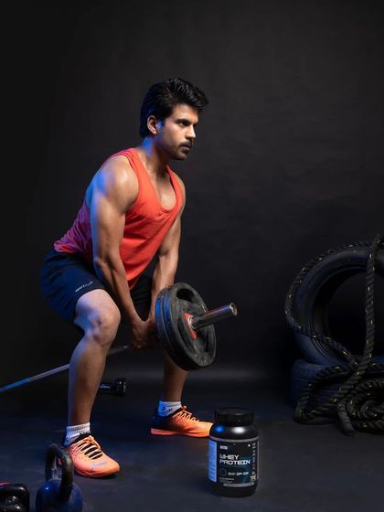 An action shot of the male model performing a bent-over row with a barbell. The supplement container is strategically placed in the foreground to be visible during the workout, linking the product to peak performance.