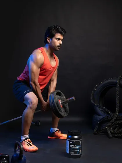 An action shot of the male model performing a bent-over row with a barbell. The supplement container is strategically placed in the foreground to be visible during the workout, linking the product to peak performance.