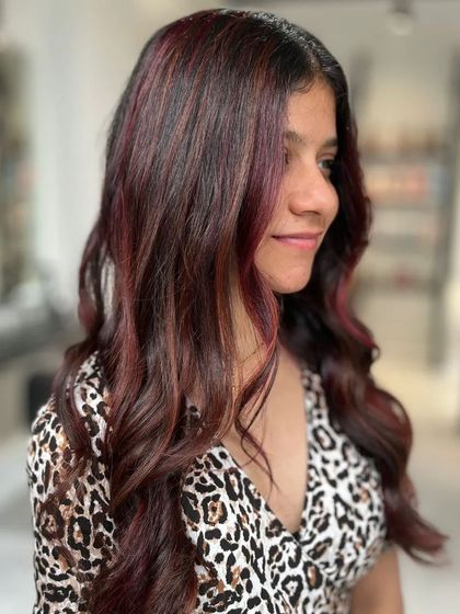 A side profile of the client, her red balayage styled into soft, elegant waves.