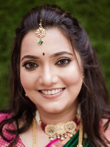 A close-up of an engagement party look. The focus is on defined eyes and a warm, smiling expression, complemented by a maang tikka.
