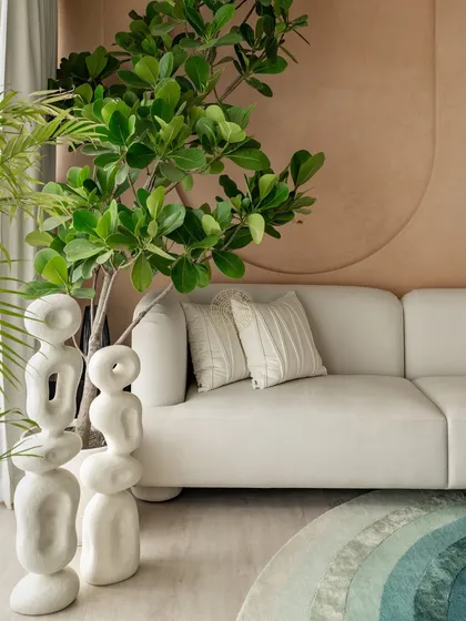 Detail shot of the living area, highlighting the clean lines of the white sofa next to abstract white sculptures. The wall behind features subtle, curved paneling that adds texture and depth to the neutral palette.