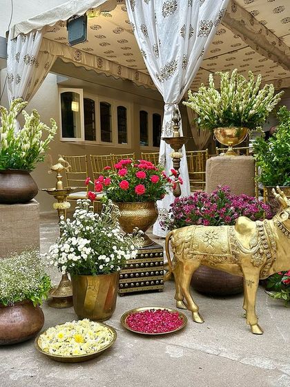 A stunning collection of traditional decor items, including a brass Nandi, antique pots filled with colorful flowers, and block-printed fabrics.