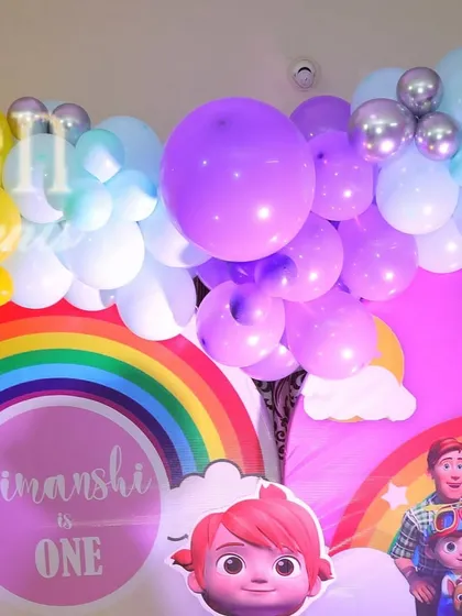 Detail of a Cocomelon party backdrop, featuring a rainbow and character cutouts. The pastel and purple balloon garland adds a soft, dreamy touch.