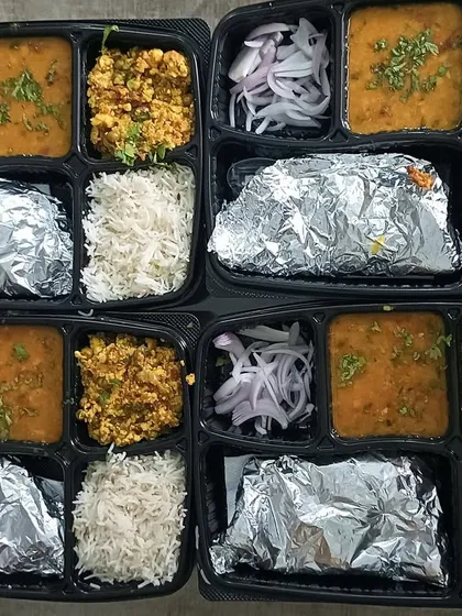 Four identical thalis prepared for a group order. This meal consisted of Paneer Bhurji, a yellow dal, steamed rice, and soft rotis, ensuring everyone gets a consistent and tasty meal.
