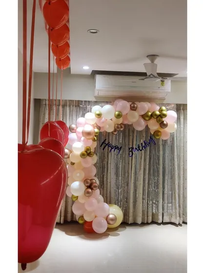 A sophisticated balloon arch for a couple's birthday party. The arch in pastel pink, white, and gold frames a shimmer curtain, creating an elegant photo backdrop.