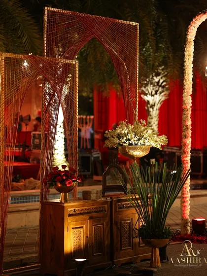 An artistic installation using red and gold thread to create arch-like structures, placed over rustic wooden cabinets.