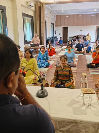 An instructor guides a large group through a Pranayama session. The focus is on controlled, mindful breathing, a cornerstone of yogic practice for calming the mind and enhancing vital energy.