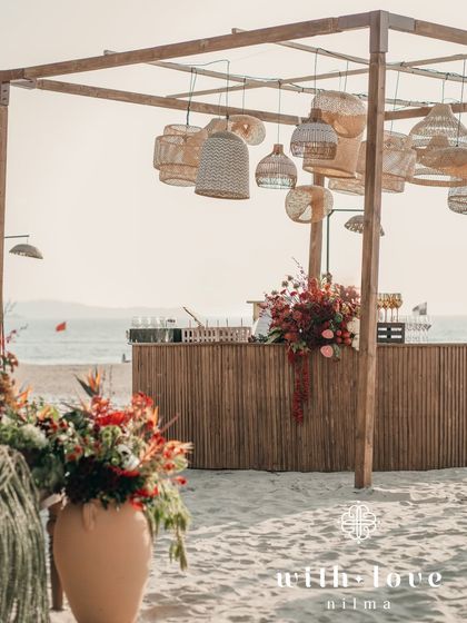 The bar area at the beach event, with rattan lamps and a backdrop of the ocean.