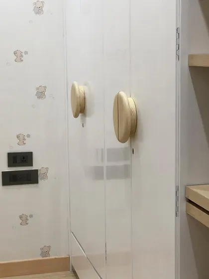 Small details make a big difference. The custom round wooden handles and subtle teddy bear wallpaper add a touch of warmth and personality to this modern, neutral nursery.