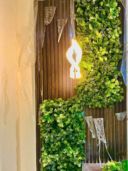 This custom installation features a flowing design of artificial moss and leaves on a wood-paneled wall, with a modern light fixture integrated directly into the greenery for a truly unique art piece.