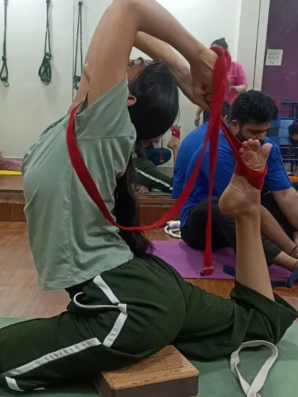This student is working on her King Pigeon Pose using a yoga belt. This prop helps in gently pulling the foot towards the head, increasing flexibility in the shoulders and quads over time.