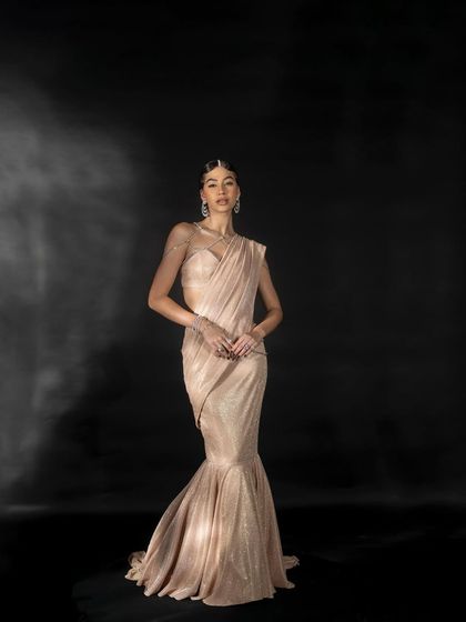 A full-length studio shot for Nikhil Thampi's 'GLEAM' collection, featuring a model in a shimmering mermaid-style gown against a dark, moody backdrop.