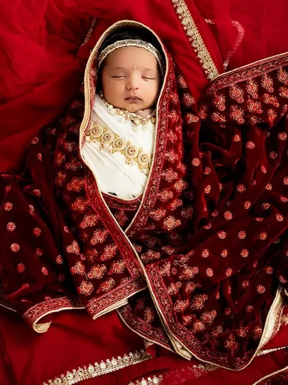 For a baby girl, I can create a beautiful Little Radha setup. Here, the newborn is wrapped in a luxurious red velvet shawl, looking like royalty.
