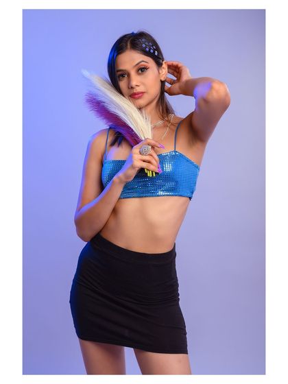A vibrant studio portrait with cool-toned lighting. The sequined top and playful pose create a fun and modern look, perfect for a party or event-themed shoot.