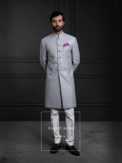 A symphony of elegance in silver-grey silk. The sherwani’s straight silhouette shines with diamond jacquard artistry, crowned with a fish-scale textured achkan.