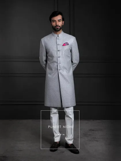 A symphony of elegance in silver-grey silk. The sherwani’s straight silhouette shines with diamond jacquard artistry, crowned with a fish-scale textured achkan.
