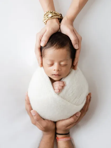 A powerful and artistic photo showing a newborn baby held securely in their parents' hands. This shot symbolizes protection, love, and the beginning of a new family unit.