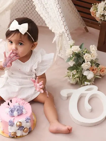 A handful of happiness. This shot, with the "One" sign and floral props, perfectly frames the birthday girl as she enjoys her cake. It’s a classic cake smash moment, full of sweetness.