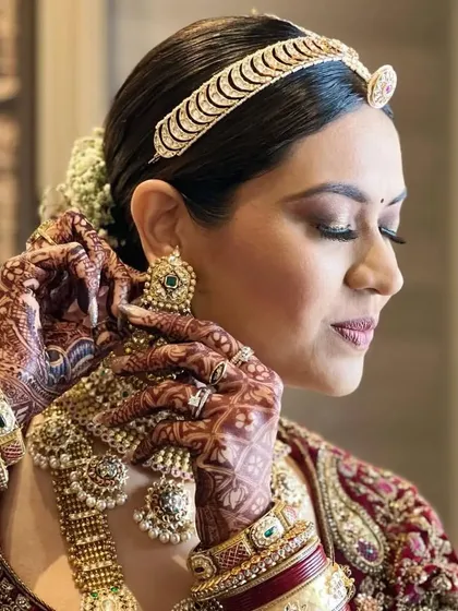 A close-up of a bride adjusting her earring, her hair styled in an elegant floral bun. This classic updo is perfect for showcasing statement jewellery.