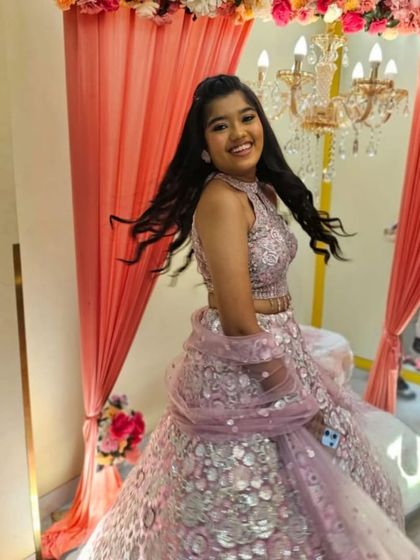 A young client looking happy and excited in a pink sequined lehenga for a family function.