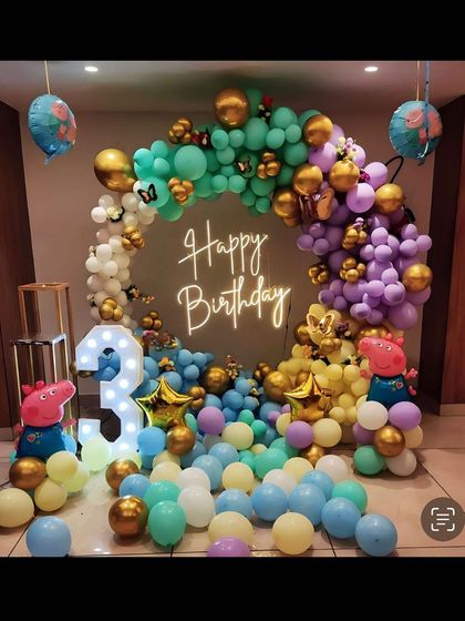 A colorful Peppa Pig themed party for a 3rd birthday. This setup features a full ring of balloons in multiple colors, Peppa Pig character stands, and a light-up number '3'.