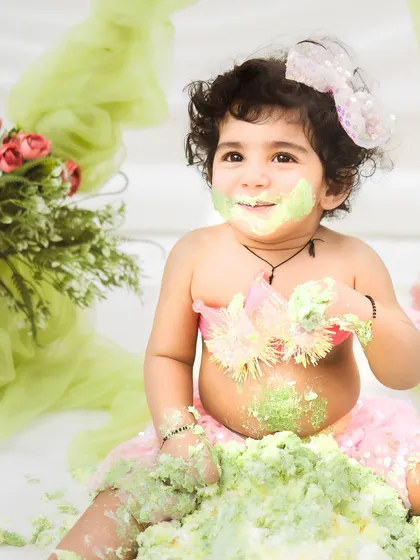 Covered in green frosting and happiness. This candid shot captures the pure delight of a baby enjoying her cake smash session to the fullest.