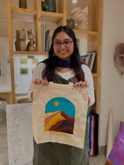 A participant proudly holds up a tote bag she painted with a modern, colorful landscape design.