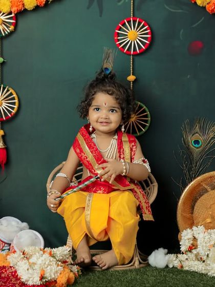 A charming portrait of a toddler dressed as Lord Krishna, sitting happily in a festive setting. We pay close attention to every detail, from the costume to the props.
