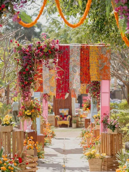 The entrance pathway to the 'Rajasthani Folklore' Mehendi, lined with colorful floral arrangements and crates.
