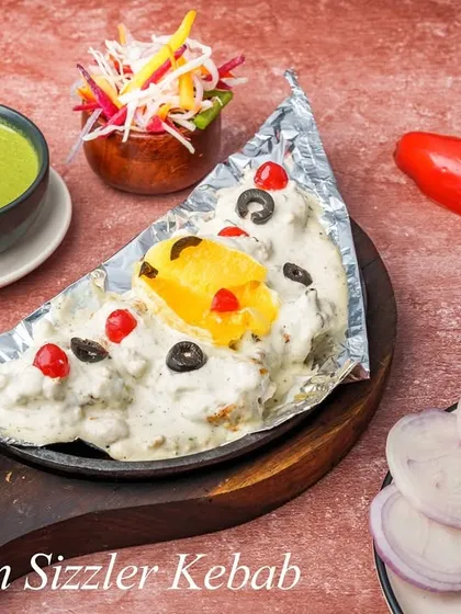 Experience our Moroccan Sizzler Kebab, a unique dish that arrives sizzling at your table. Tender kebabs are stuffed with our chef's special filling, smothered in a creamy Moroccan sauce, and garnished with olives, cherries, and a slice of mango for a sweet and savory fusion.