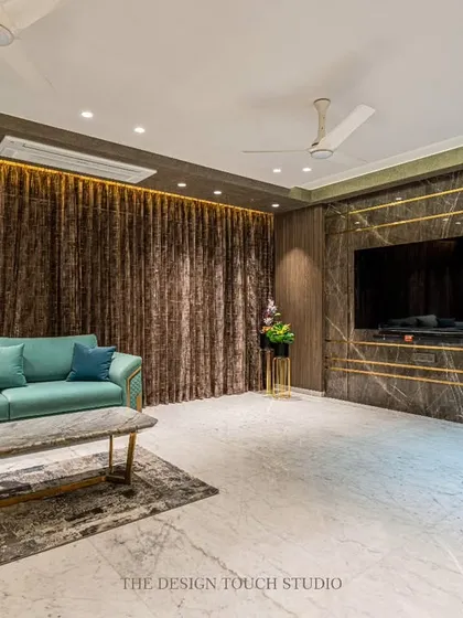 The TV wall in this living room is a statement of understated luxury, featuring a dark marble panel with inlaid gold-finished metal strips. This design element adds a touch of glamour without overwhelming the space.