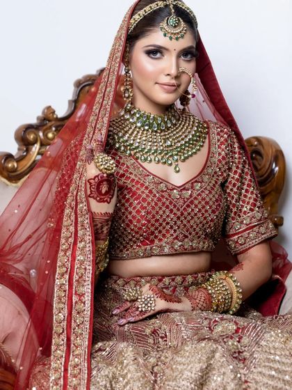 A full portrait of the bride, showcasing her beautiful red and gold lehenga and the complementary makeup.